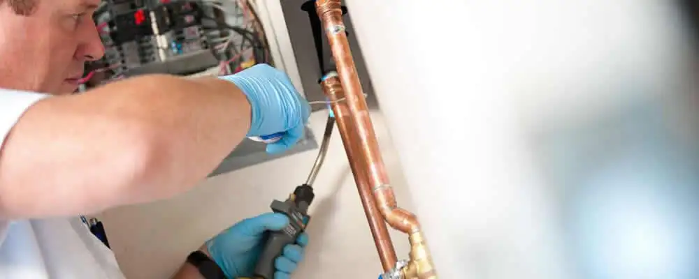 Water heater repair technician testing copper pipe connections and controls in Pasadena, CA